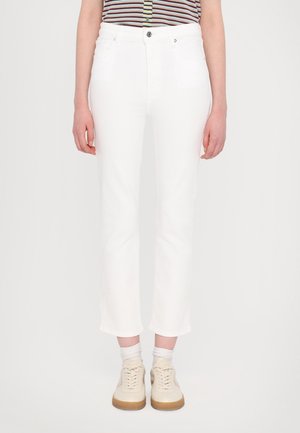 Person wearing white cropped pants, light beige sneakers with white socks, and a striped shirt with buttons visible.