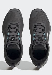 Scarpe da ginnastica nere con tomaia in rete testurizzata, lacci turchesi a contrasto e tallone rinforzato. Presentano un colletto imbottito e un dettagli del logo.