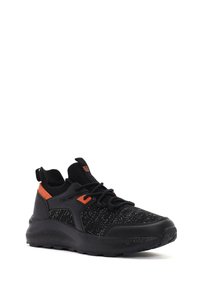 Bottine de sport noire en tissu tricoté texturé avec une semelle en caoutchouc, ornée d'accents orange, de lacets et d'une languette à l'arrière.