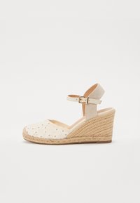 Sandalia de cuña con parte superior de tela crema que presenta bordados florales, un tacón de yute trenzado y una correa ajustable en el tobillo de lona beige.