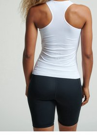 Top sportivo bianco attillato con design a racerback, abbinato a pantaloni corti neri a vita alta. Texture liscia, stile minimalista.
