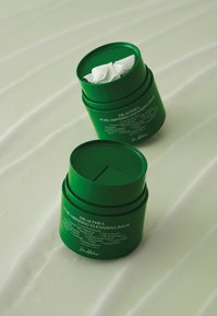 Zielony, okrągły pojemnik z balsamem oczyszczającym Dr. Althea Pure Grinding z fakturowaną pokrywką i wytłoczonym napisem; zawiera wyjmowaną wewnętrzną wkładkę.