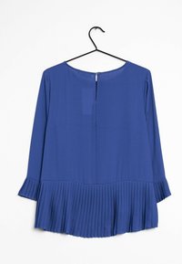 Blusa blu con maniche lunghe, orlo inferiore plissettato e scollo rotondo. Il tessuto appare liscio con un leggero lucido. Chiusura posteriore con bottoni.