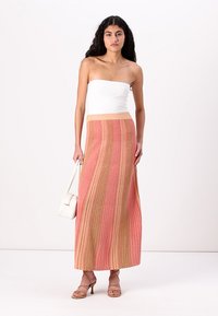 Jupe maxi rayée en rose et beige avec une texture verticale, associée à un haut sans manches blanc et des accessoires de couleur claire.