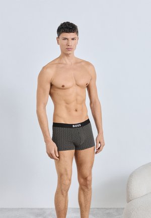 Schwarz-weiß gemusterte Boxershorts mit einem schwarzen Bund, auf dem der Markenname "BOSS" deutlich zu sehen ist.