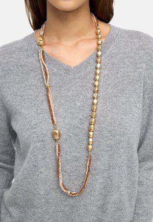 Kobieta nosząca długi naszyjnik z nieregularnymi złotymi koralikami oraz małymi brązowymi i beżowymi koralikami, na jasnoszarym swetrze z dekoltem w serek.