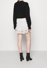 Pull noir oversize, jupe blanche à volants avec motif tacheté noir, et bottines noires à talons avec détail texturé.