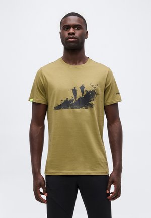 Rövid hajú férfi, aki mustár színű pólót visel, amelyen két terepfutó fekete grafikája és egy kis logó található a mellkason.