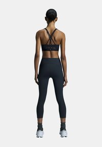 Zwarte sportbeha met kruislings gesneden bandjes, gecombineerd met hoge zwarte leggings en witte sportschoenen. Glad textuur, nauwsluitend ontwerp.