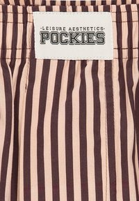 Roosad ja tumedat pruuni triibulised lühikesed püksid, millel on kokku kogutud vöökoht. Näitusel valge silt, millel on tekst "LEISURE AESTHETICS POCKIES".
