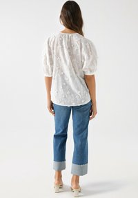 Hvid broderet bluse med pufærmer, parret med blå denimjeans med en frayed kant og lyse denimcuff.