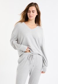 Szara bluza z dekoltem w serek i długimi, luźnymi rękawami, zestawiona z pasującymi spodenkami dresowymi na sznurku. Miękka, teksturowana tkanina.