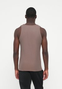 Brun tætsiddende tanktop med ribbet tekstur, smalle skulderstropper og en afrundet udskæring, båret med sorte shorts.