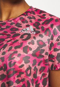Camiseta deportiva de manga corta en negro y rosa con estampado de leopardo y textura de malla; presenta el logotipo plateado de Adidas en el pecho.