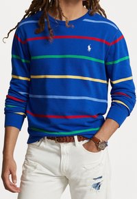 Camisa de manga larga azul con rayas horizontales en rojo, verde, amarillo y azul; presenta un cuello redondo y un pequeño logo en el pecho.