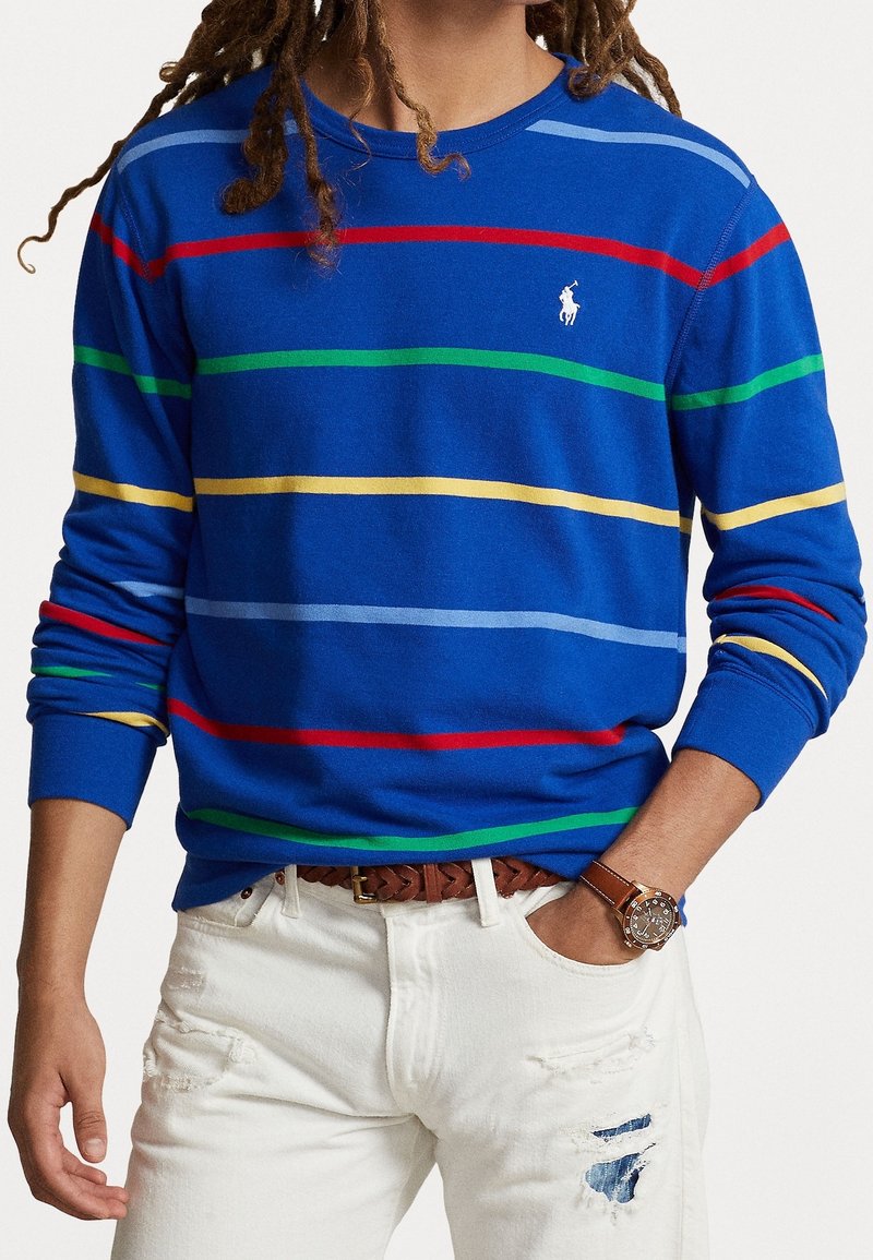 Camisa de manga larga azul con rayas horizontales en rojo, verde, amarillo y azul; presenta un cuello redondo y un pequeño logo en el pecho.