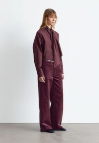 Maroon shirt with a tie detail paired with wide-leg maroon corduroy pants. Smooth texture, minimalist design. Black pointed-toe shoes.