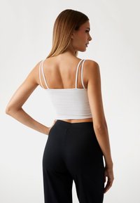 White cropped tank top with double thin straps, fitted design, paired with high-waisted black trousers. Smooth, stretchy fabric.