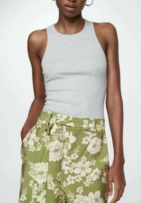 Grijze mouwloze top van ribstof, gecombineerd met groene broek met bloemenprint, voorzien van een strikceintuur en zijzakken.