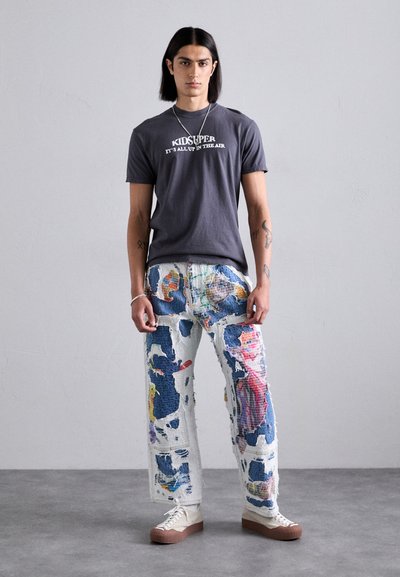 Gray cotton t-shirt with "KIDSUPER IT'S ALL UP IN THE AIR" text, paired with multicolored, patched denim jeans featuring a distressed design.
