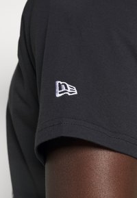 Černé bavlněné tričko s krátkými rukávy, na rukávu s vyšívaným bílým logem, které ukazuje hladkou texturu a čisté švy.