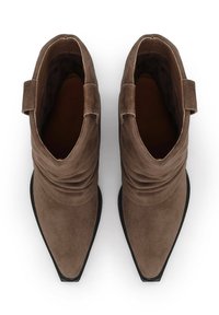Botas de tobillo de ante marrón con un diseño holgado y punta afilada. Presentan una textura suave y una suela de goma negra.