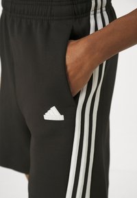 Black athletic shorts with elastic waistband, featuring white side stripes and an Adidas logo on the left leg. Smooth fabric texture.