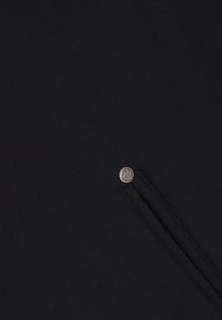 Der schwarze Pulloverstoff weist eine strukturierte Oberfläche auf, mit einem kleinen silbernen Knopfdetail in der Nähe eines Reißverschlusses an der Seite.
