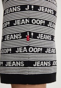 Maglione a maglia con un motivo testuale ripetuto in bianco e nero. Presenta strisce grigie e una piccola etichetta rossa di accento sul lato.