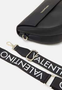 Borsa Valentino in pelle nera con tracolla nera removibile, caratterizzata dal logo Valentino bianco e hardware dorato, su sfondo bianco.