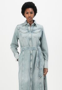 Denim shirt dress, light blue, long sleeves, button front, two chest pockets, cinched waist with a matching belt, side slits.