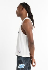 White mesh athletic tank top with a loose fit, featuring contrasting black logo and horizontal stripes on the shorts, paired with a simple design.