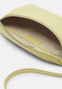 Żółta skórzana kopertówka z zamkiem błyskawicznym i gładką, matową teksturą. Wnętrze wykończone jasnym materiałem i małą metką z logo.