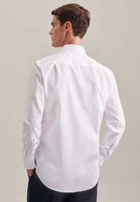 Witte langarmshirt met een klassieke kraag, rugplooien en knoopmanchetten. De stof heeft een gladde textuur, met een getailleerd ontwerp en een gebogen zoom.