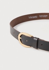 Melnā brūnā krāsā pārklāts ādas josta ar gludu tekstūru, ar zelta krāsas ovālu sprādzi un vairākiem regulēšanas caurumiem.