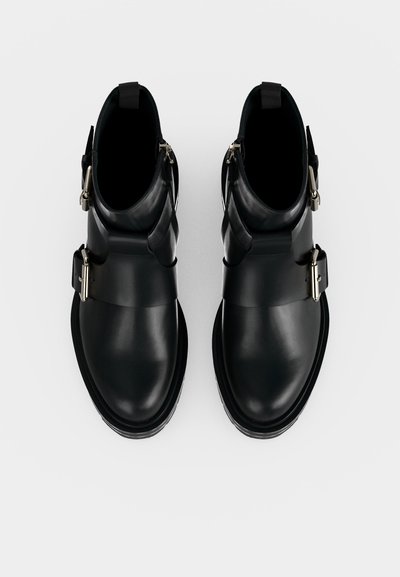 Paire de bottines en cuir noir avec boucles latérales argentées et bouts ronds vues de dessus sur fond blanc.