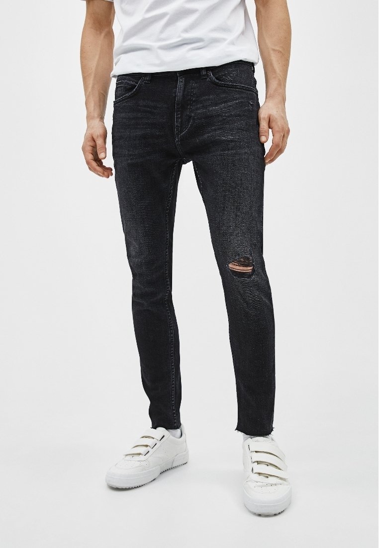 Jeans negros de corte ajustado hechos de denim, con un detalle de rodilla rasgada y un acabado desgastado, combinados con zapatillas blancas.