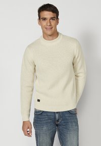 Crème kleurige gemêleerde gebreide trui met een ronde hals, lange mouwen en een klein bruin logo label aan de zoom. Gekocht met spijkerbroek.