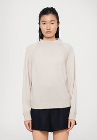 Maglione beige chiaro con collo alto, maniche lunghe e orlo a coste. Texture morbida a maglia, con cuciture raglan per una vestibilità rilassata.