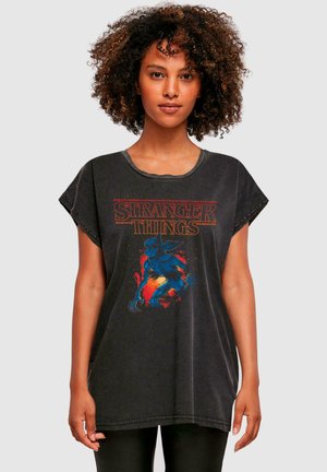 Mustat ylisuuret t-paidat, joissa on punainen "Stranger Things" -logo ja sinisen olennon kuvitus eloisilla taustatiedoilla.