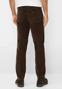 Braune Cordhosen im Slim Fit, mit Gesäßtaschen und einer strukturierten Oberfläche. Kombiniert mit dunklen Schuhen für den Kontrast.