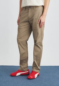 Μπεζ βαμβακερό παντελόνι με ευθεία γραμμή, διαθέτει κλείσιμο με κουμπί και τσέπες, συνδυασμένο με κόκκινα αθλητικά παπούτσια.