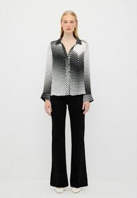 Camicia button-up bianca e nera con un motivo a punti in gradiente, maniche lunghe e colletto ripiegato, abbinata a pantaloni neri a zampa.