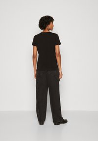 Crna kratka majica s kratkim rukavima u kombinaciji s labavim crnim cargo hlačama. Outfit se odlikuje glatkom teksturom i minimalističkim dizajnom bez uzoraka ili detalja.
