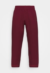 Maroon athletic pants with elastic waistband, featuring contrasting red stitching and a small black Nike logo on the upper left leg.
