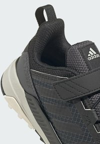 Zapatilla deportiva negra con parte superior texturizada, correa de velcro y suela gris en contraste. Presenta el logotipo de Adidas Terrex y un diseño elegante.