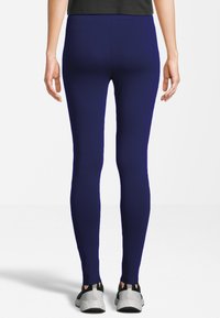 Leggings azul marino hechos de una tela elástica, con un diseño ajustado y aberturas en los tobillos. Combinados con zapatillas deportivas grises y negras.