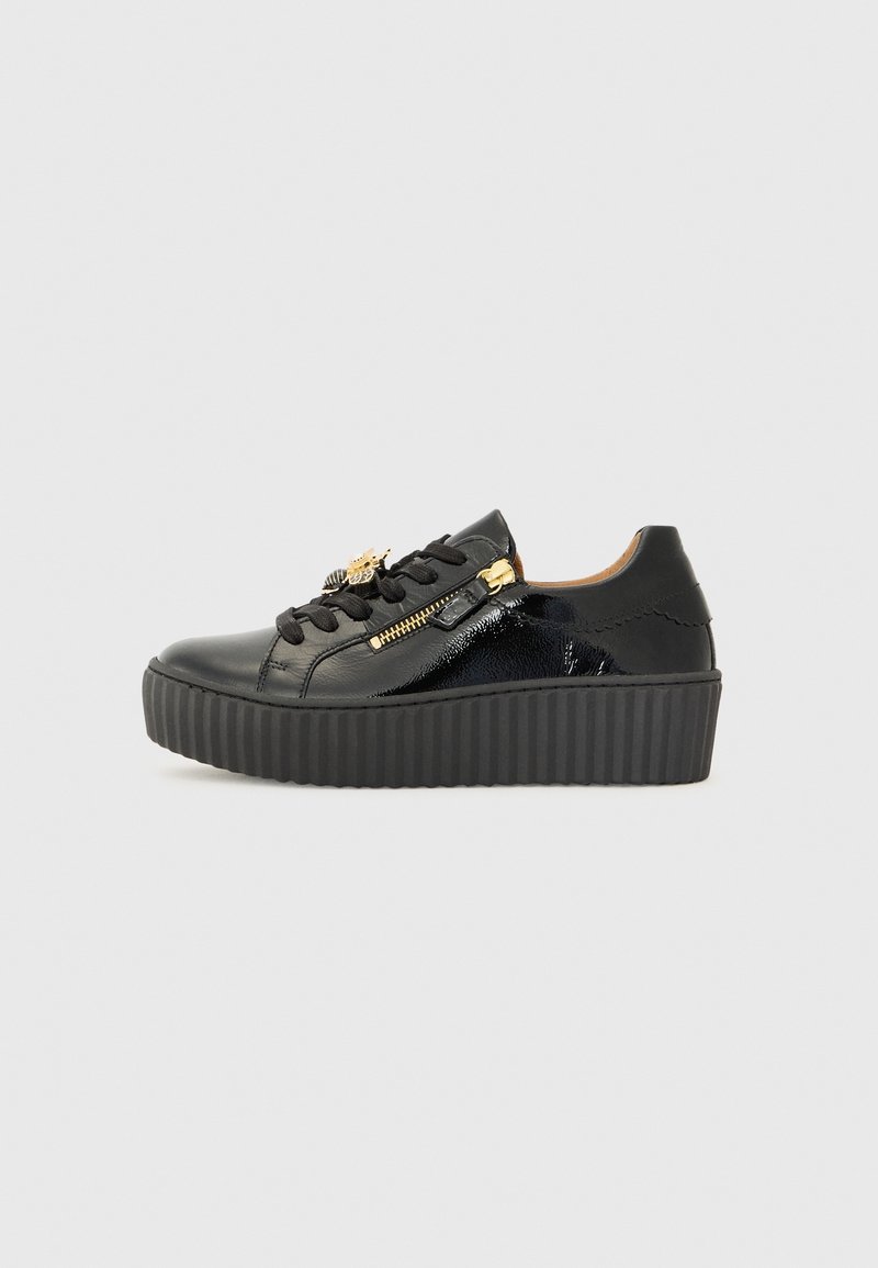 Baskets à plateforme noires avec semelle épaisse rainurée, détails en cuir brillant, lacets noirs, fermeture éclair dorée et charm en forme d'abeille sur le côté.