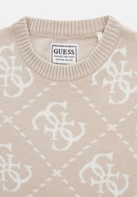 Maglione a maglia beige con un motivo a rombi, decorato con loghi bianchi. Collo a girocoscia a coste. L'etichetta riporta "GUESS EST. 1981 DESIGN ORIGINALE."