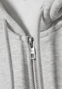 Sweat-shirt à capuche gris avec une texture lisse et une fermeture éclair métallique à l'avant, doté d'un cordon tressé à la capuche.